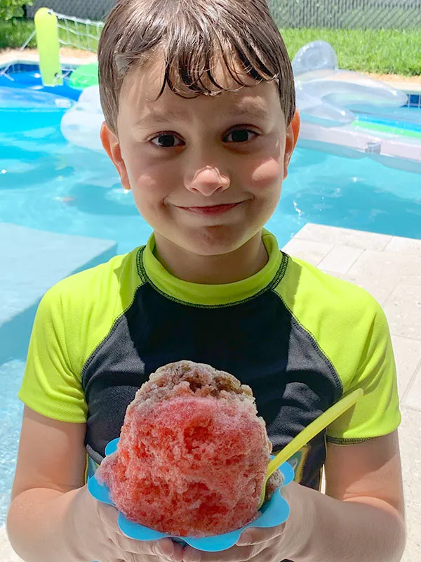 Boy at a pool party holding a shave ice