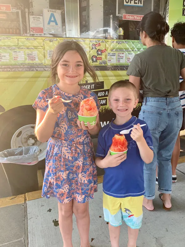 Two kids holding shave ice in front of a shave ice truck